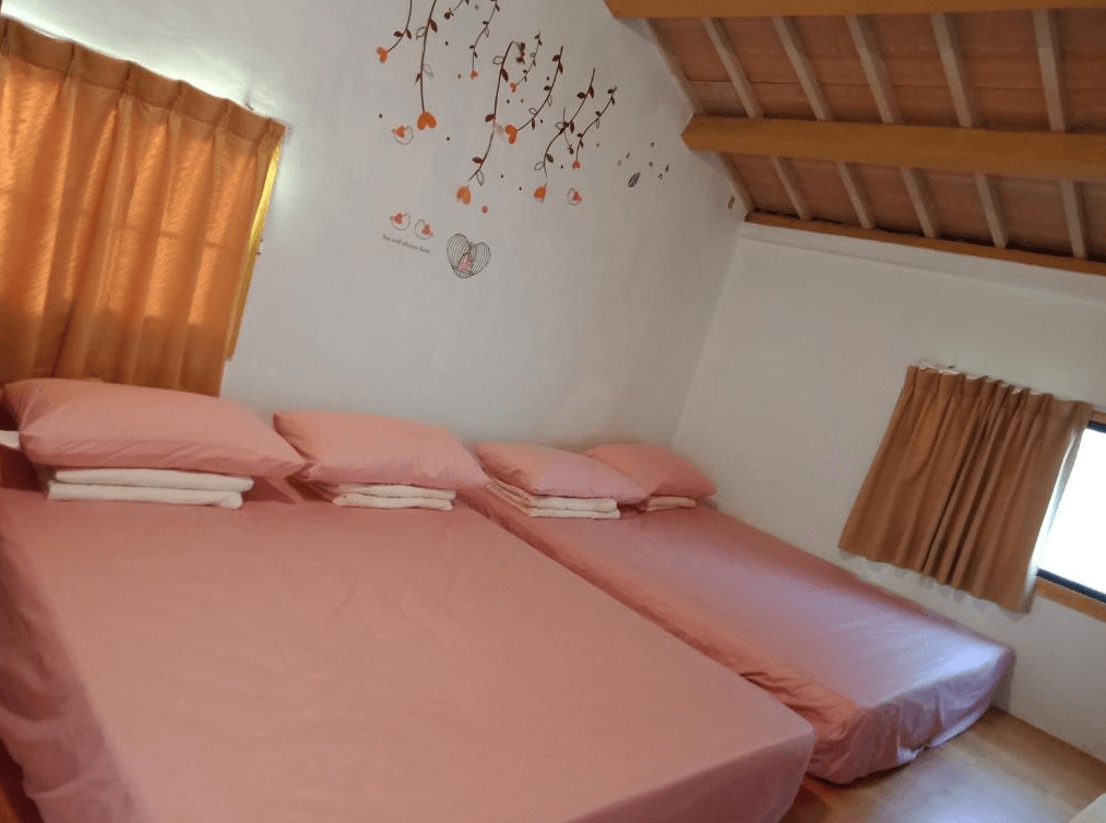 【嘉義寵物友善住宿】船仔頭天賞居民宿的多人房，牆面裝飾有簡約樹枝和愛心圖案，房內鋪設三張粉色床墊，搭配橘色窗簾和木樑天花板，營造溫馨舒適的氛圍。