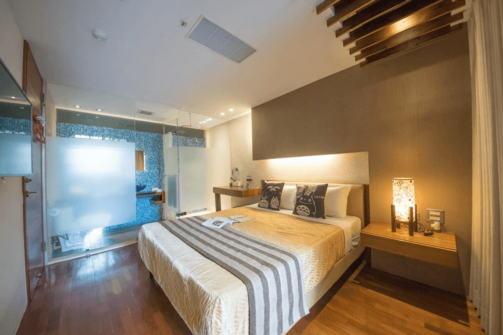 【日月潭住宿】苔米屋的房間延續木質與暖色調設計，浴室採用透明玻璃隔間搭配藍色馬賽克牆，營造清新現代的視覺效果。床頭兩側設有柔和的燈光，增添舒適與溫馨氛圍。