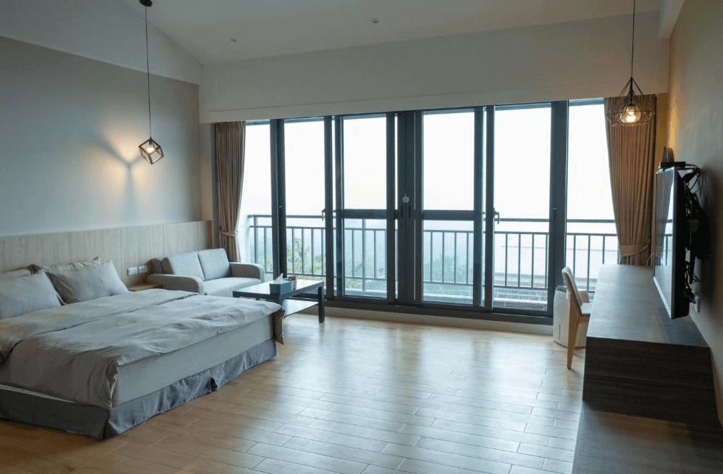 【阿里山住宿】茶緣觀舍寬敞的現代化客房，設有落地窗與陽台，提供極佳的自然光線與視野。房間內有雙人床與舒適的沙發區，木質地板增添溫暖的氛圍，整體設計簡約而雅緻。