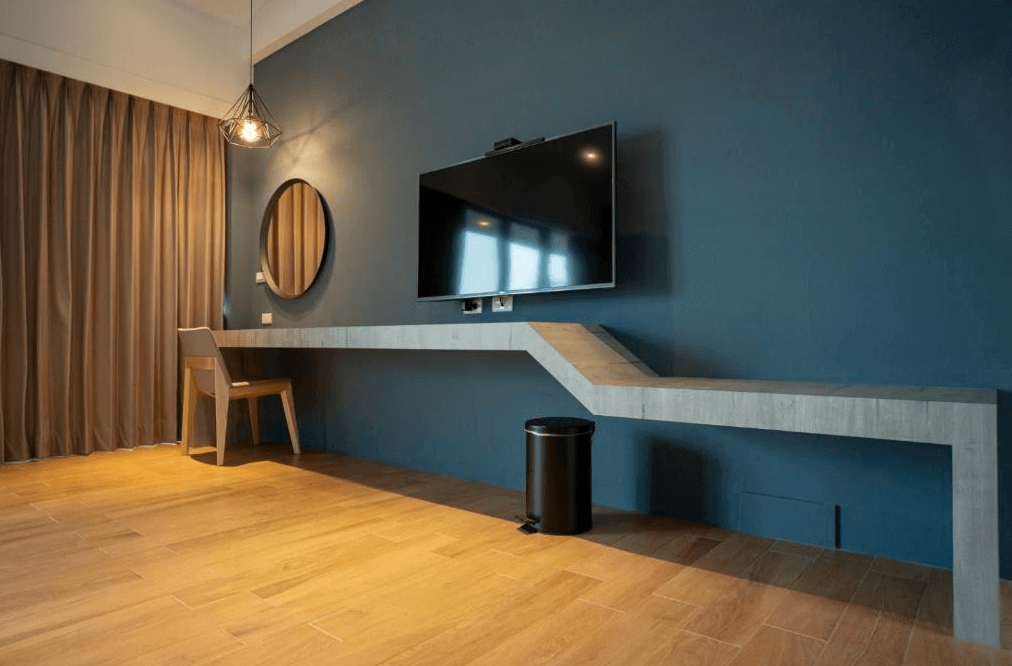 【阿里山住宿】茶緣觀舍設計感十足的藍色牆面搭配創意書桌與掛牆式平板電視，提供實用的工作與娛樂空間。圓形化妝鏡與簡約木椅增加細節美感，整體風格沉穩又不失時尚。