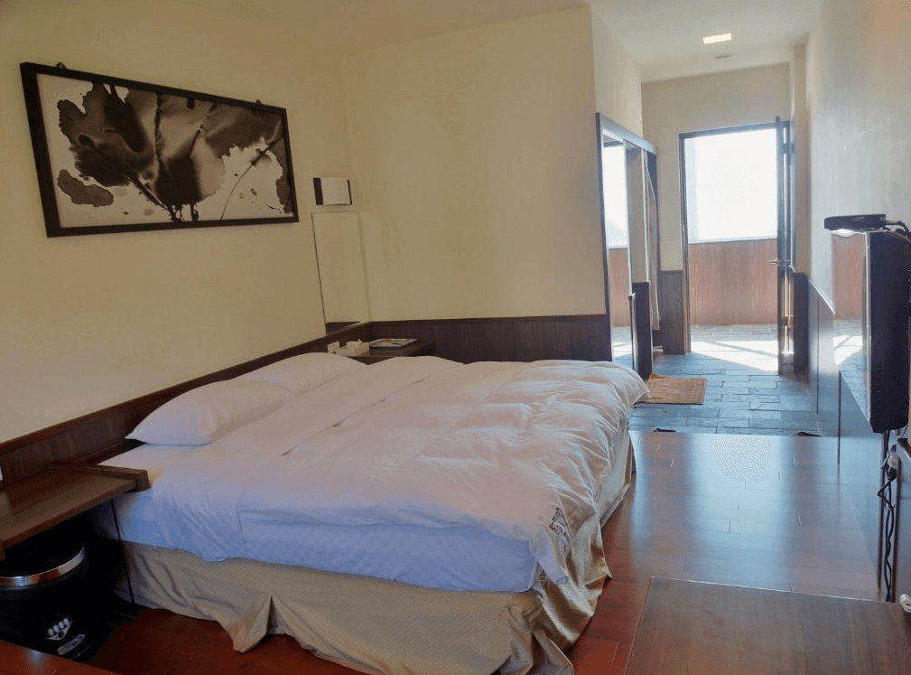 【阿里山住宿】茶雲居的房間設計簡潔，以木質地板與白色牆面為主，營造溫暖的住宿氛圍。窗外明亮的自然光線讓空間更加舒適，房內設有雙人床與基本家具，適合簡單入住需求。