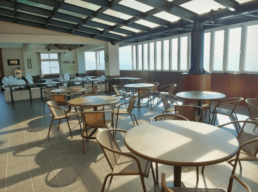 【阿里山住宿】茶雲居明亮的餐廳空間以大片窗戶為特色，讓旅客能一邊用餐一邊欣賞壯麗的山景。餐桌與座椅配置簡潔實用，適合團體聚餐或個人休憩。