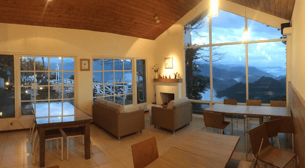 【阿里山住宿】茶香花園民宿設有大面積的落地窗，外景如畫般迷人。客廳內有沙發區與餐桌，讓住客可在此放鬆或享用餐點。木質屋頂增添溫暖感，適合聚會或閱讀。