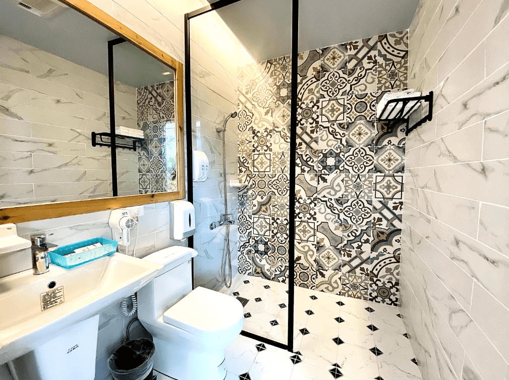 【阿里山住宿】茶香花園民宿的浴室設計時尚，牆面採用花磚與大理石紋理，融合古典與現代風格。乾濕分離的設計提升便利性，搭配木框鏡子與簡約衛浴設施，展現精緻舒適的空間感。