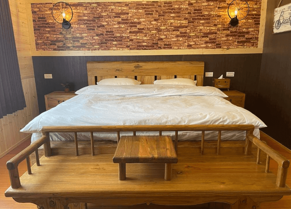 【司馬庫斯住宿】薔薇谷的鄉村木質風格的客房，主體為一張大尺寸木製床，牆面裝飾有紅磚圖案與黑色金屬燈具，床頭兩側擺放著木製床頭櫃，營造出溫暖且樸實的氛圍。