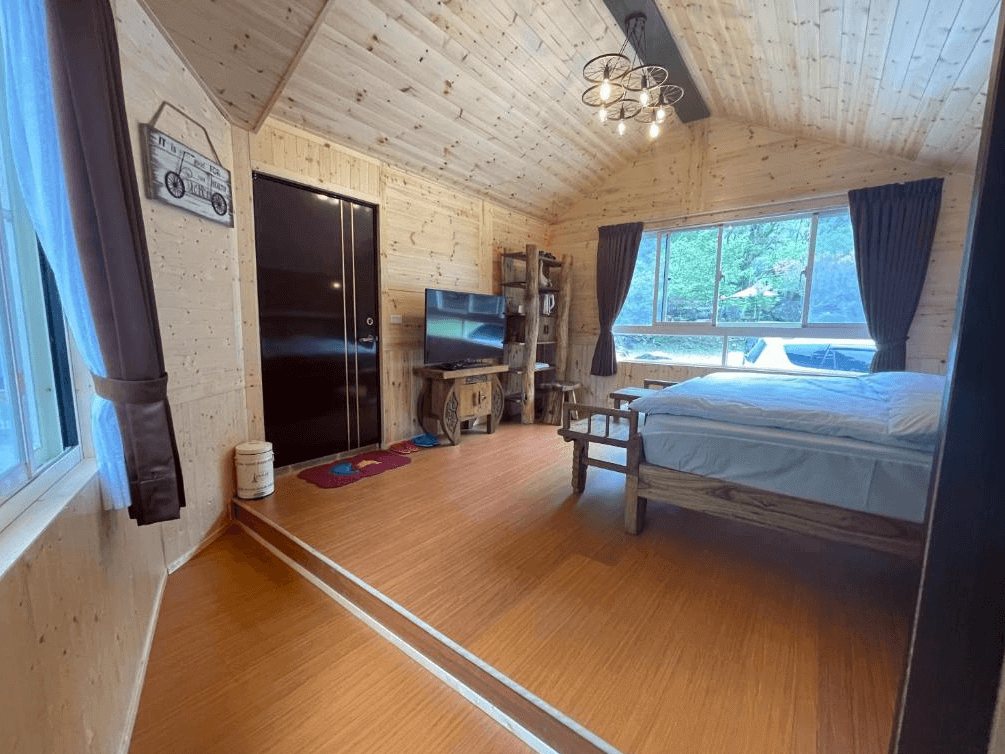 【司馬庫斯住宿】薔薇谷的木屋房間，內部裝飾大量木質元素，包括牆壁、天花板與家具，房內有一張大床、電視及窗戶透入自然光，窗外可見綠意盎然的景色，整體空間舒適且具有自然氣息。