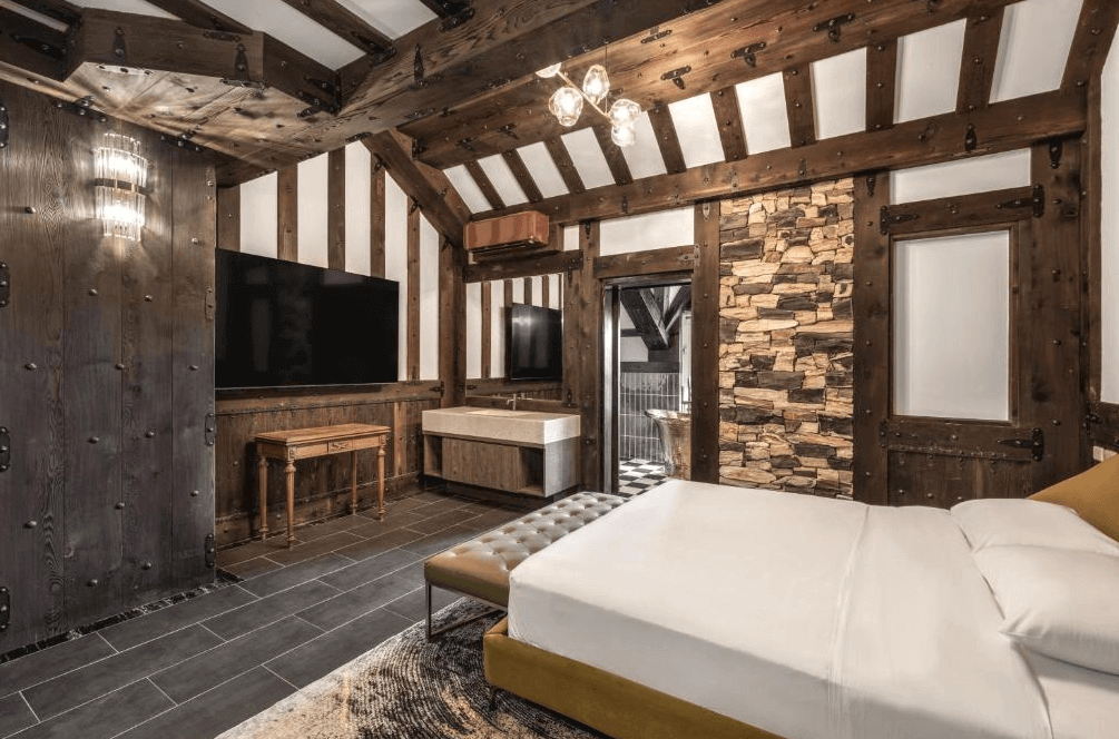 【埔里住宿】藍色城堡茱諾法式甜點的裝潢以木質元素為主，牆面和天花板呈現古典樑柱設計，搭配石材裝飾，增添溫暖質感的同時兼具現代感。房間內的家具包括舒適的沙發和大尺寸電視，營造出豪華的居住氛圍。