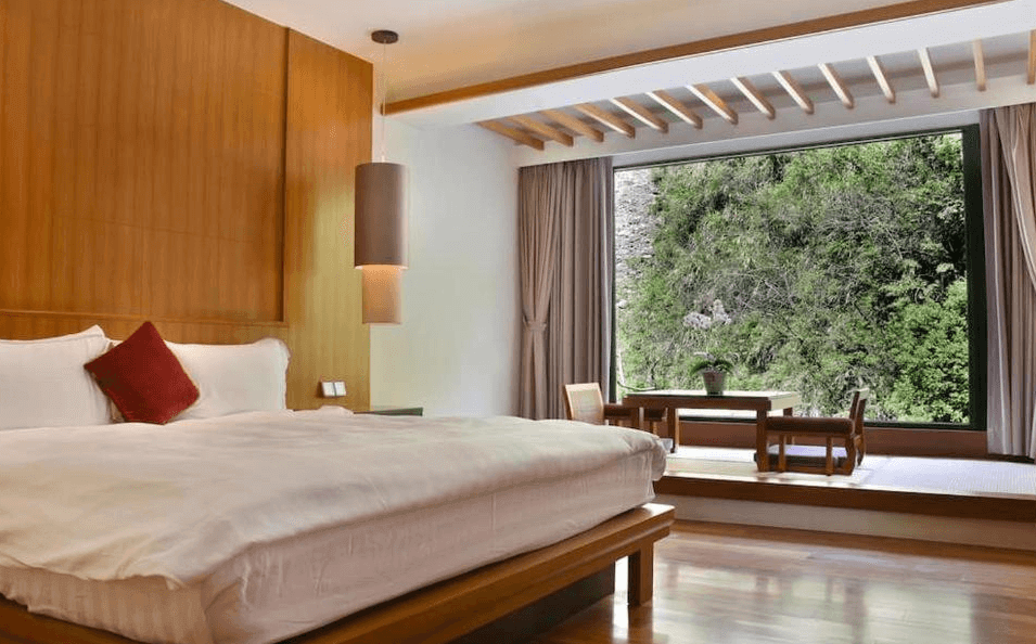 【廬山溫泉】蜜月館大飯店和風設計的豪華雙人房，搭配木質裝潢與簡約吊燈，展現自然質感。房內擁有加大雙人床，靠窗區設有和式桌椅，大片落地窗帶來充足自然光，可欣賞綠意盎然的山景，營造寧靜悠閒的住宿氛圍。