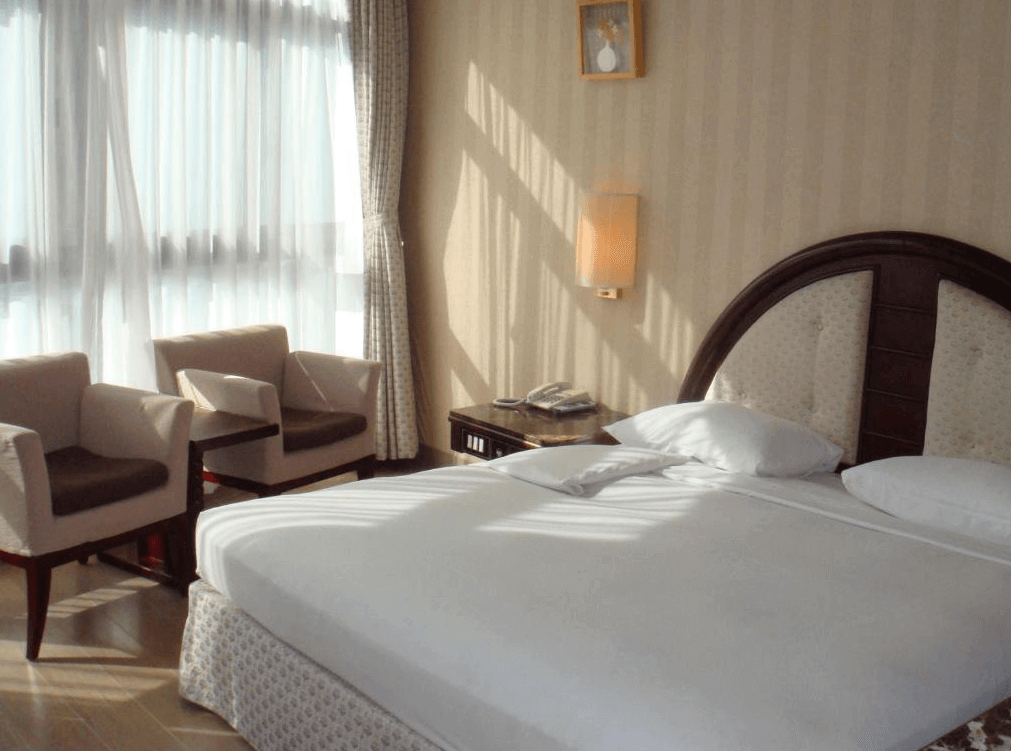 【廬山溫泉】蜜月館大飯店典雅風格的雙人房，搭配柔和色調的壁紙與木質家具，營造溫馨舒適的氛圍。房內設有大床、雙人沙發座椅與小茶几，大片窗戶讓房間充滿自然光線，適合享受悠閒時光。