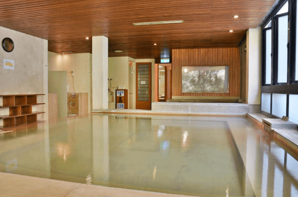 【廬山溫泉】蜜月館大飯店寬敞的溫泉大眾池，室內設計融合木質與石材元素，展現典雅的日式溫泉風格。溫泉水清澈透亮，牆面裝飾掛有自然景觀畫，提供放鬆療癒的泡湯體驗，適合旅客享受寧靜時光。