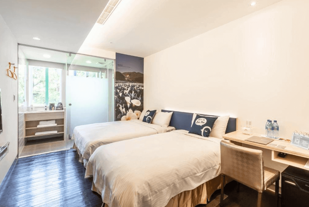 【寧夏夜市住宿】西悠巢旅-台北館一間雙床房，設計簡約，配有兩張白色床鋪，房間內的玻璃隔間浴室可看到窗外綠意景觀，牆上有自然風景的壁畫，空間明亮舒適。