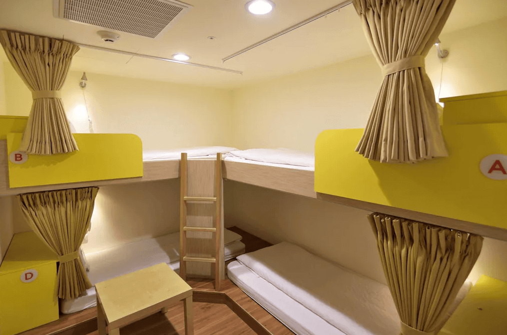 【寧夏夜市住宿】西悠巢旅-台北館的宿舍房內設有四張上下鋪床位，搭配黃色床頭板和拉簾設計，提供隱私與便利，空間整潔，採用溫暖的木質地板。
