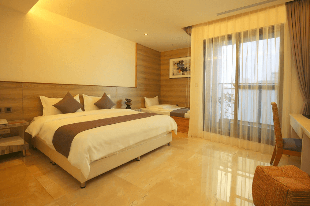 【新竹火車站住宿】達龍商旅的房間內設有一張大床及單人床，採用相同的柔和棕色調抱枕和床單裝飾，營造一致的設計感。窗戶面積大且通透，搭配半透明窗簾，讓光線柔和灑入，地面採用光滑大理石材質，展現簡潔時尚的設計。