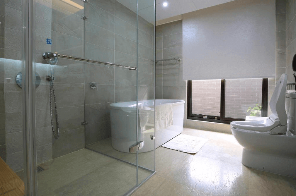 【新竹火車站住宿】達龍商旅的浴室內設有乾濕分離淋浴間與一個現代化浴缸，牆壁和地面採用淺灰色瓷磚，整體風格簡約大方。窗戶提供自然光線，讓空間顯得更加寬敞明亮，洗手台和衛生設備一應俱全，設計注重細節與實用性。