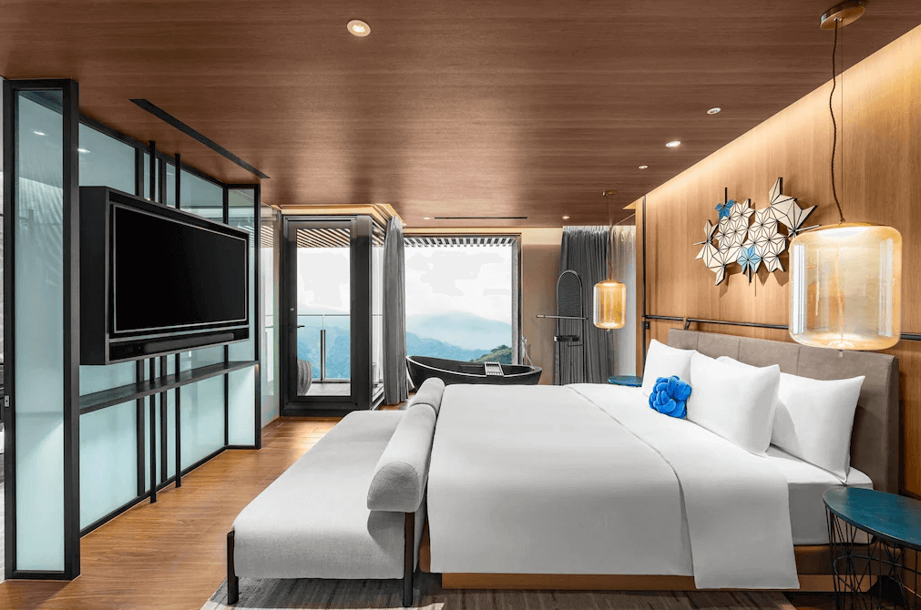 【阿里山住宿】阿里山英迪格酒店的雙人房內設有大床與精緻的軟墊沙發，室內採用木質牆面與金屬燈飾點綴，極具現代感。陽台外可欣賞廣闊的自然景色，讓住客獲得全方位的放鬆體驗。
