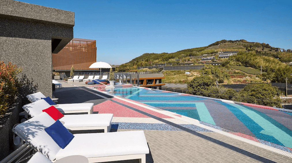 【阿里山住宿】阿里山英迪格酒店的戶外泳池擁有多彩的馬賽克設計，結合周圍的山景，視覺效果令人驚艷。旁邊設有休憩的日光椅，讓住客在享受泳池的同時能放鬆心情，體驗極致的度假氛圍。