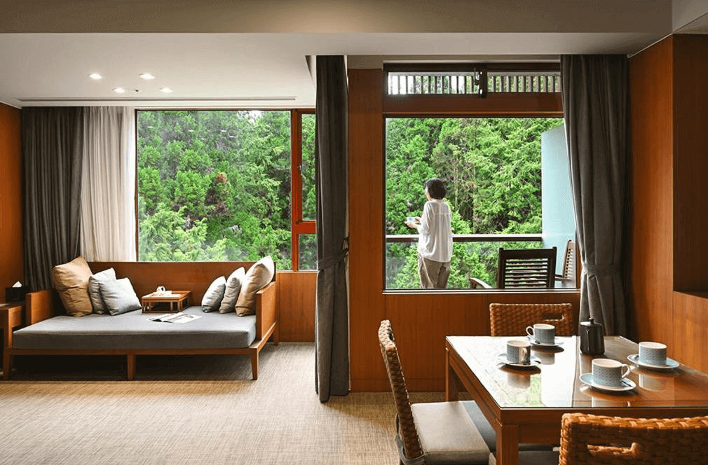 【阿里山住宿】"台灣最貴飯店"阿里山賓館寬敞的客廳區域，玻璃落地窗讓住客可以直接欣賞窗外森林景觀，提供舒適的座椅與用餐區，是放鬆身心的理想場所。