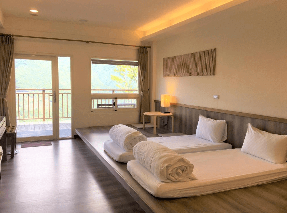 【司馬庫斯住宿】雲山房的日式風格房間，擺放兩張地墊床，旁邊有落地窗與陽台，可欣賞綠意盎然的山景，室內採用木質地板與暖色調燈光，營造出舒適的居住氛圍。
