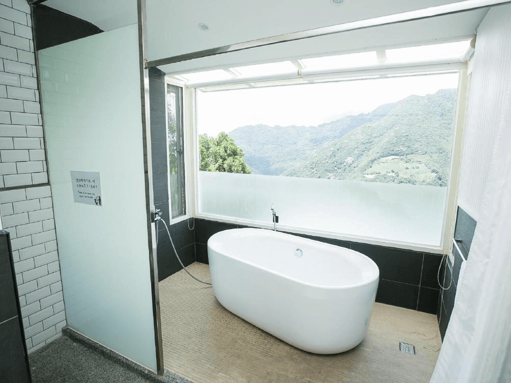 【司馬庫斯住宿】雲山房開闊視野的浴室，內設獨立式白色浴缸，窗外可欣賞青山景色，牆面以白磚與玻璃設計，結合自然與現代元素，提供放鬆舒適的沐浴體驗。