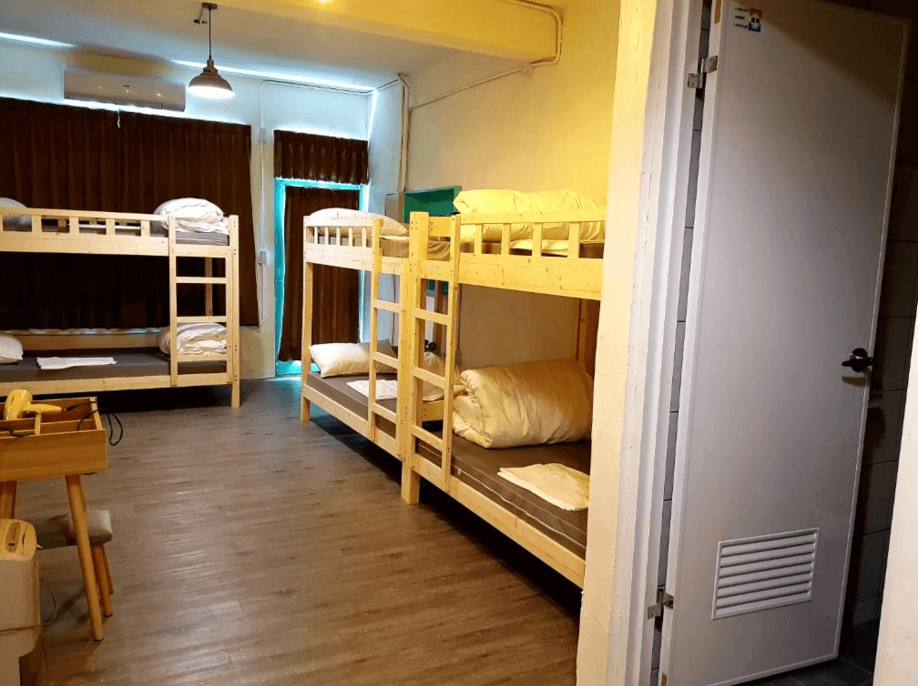 【埔里住宿】麋路背包客的背包客多人房，內部設有兩排木質雙層床，每個床位配有白色床單和枕頭。房間燈光柔和，搭配深色窗簾營造溫暖的休息空間，適合團體或個人住宿。