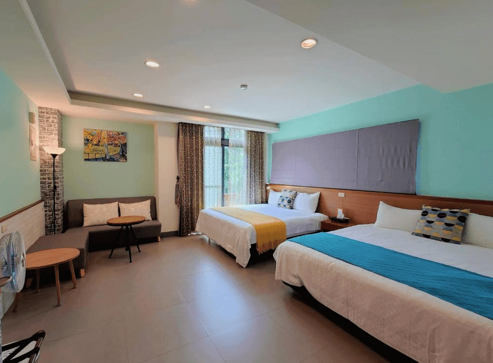 【集集火車站住宿】倍詩泰民宿的雙床房，擁有現代感的藍綠色牆面與木質裝飾，兩張舒適的大床鋪上鮮豔的床巾，搭配溫馨的抱枕。房間內設有沙發、落地燈與掛畫，大片窗戶提供自然採光，營造明亮舒適的住宿氛圍。