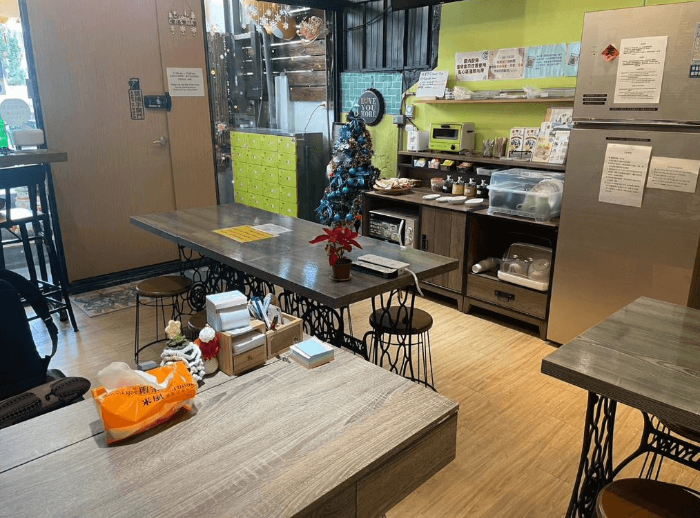 【鹿港住宿】公園一鹿背包客棧的共享廚房區域，這裡有兩張長桌和一些高腳椅，環境舒適，適合住客聚會或自行準備餐點。廚房區的設計簡單而實用，並且配有冰箱、微波爐等設備，方便住客使用。