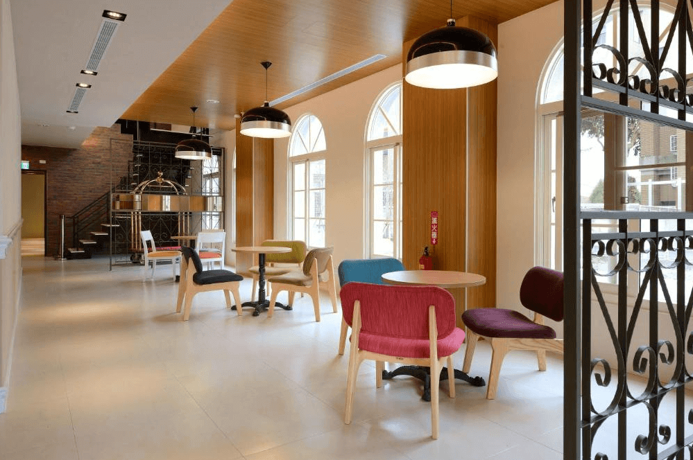 【集集火車站住宿】卡菲爾花園飯店時尚溫馨的餐飲區，設有多組色彩繽紛的座椅，搭配木質裝潢與拱形窗戶，呈現歐式鄉村風情。開放式空間設計使整體氛圍更加溫暖明亮，非常適合旅客在此享受早餐或下午茶時光。