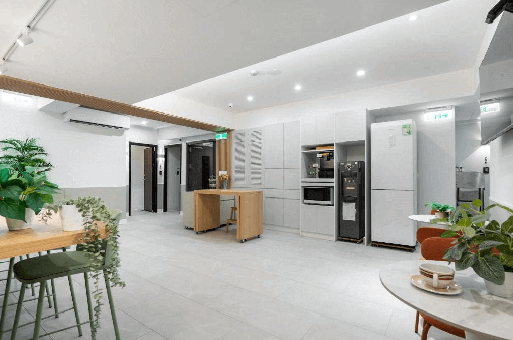 【台北車站住宿】"台北車站青年旅館"台北109青旅的共享廚房與休憩空間，內部裝潢簡約明亮，配備大型冰箱、微波爐、飲水機與烹飪設備。開放式用餐區設有高腳椅與綠色植栽裝飾，營造溫馨氛圍。