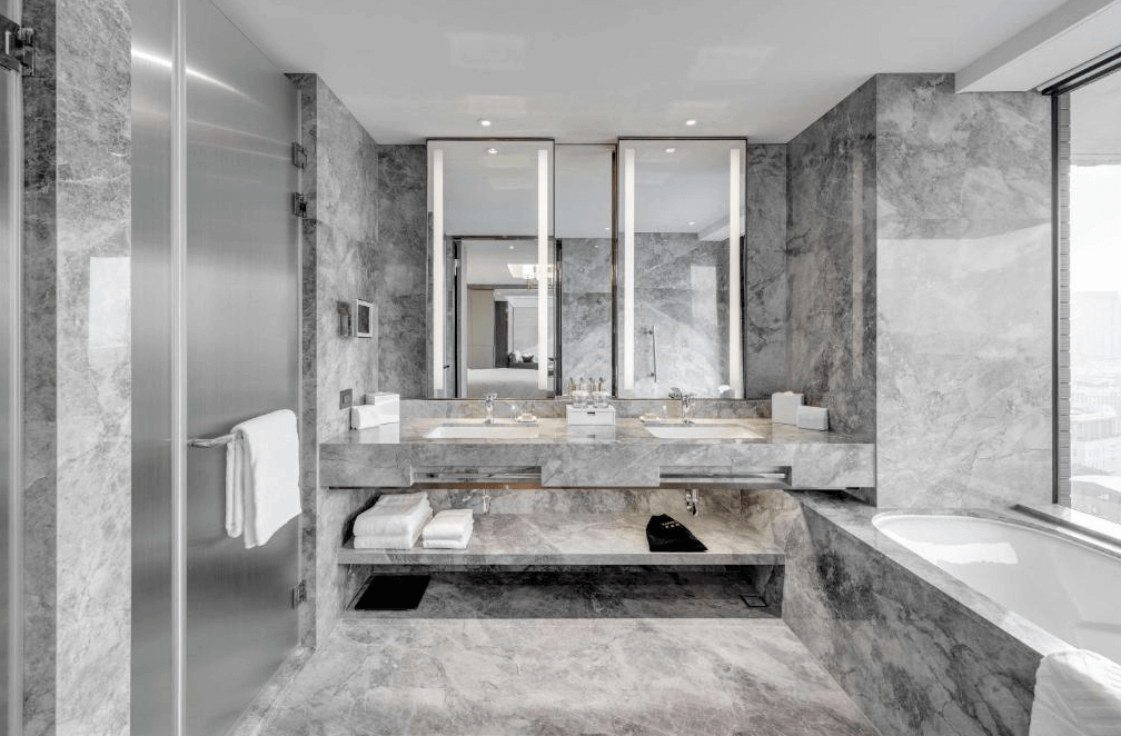 【台北車站住宿】台北中山九昱希爾頓逸林酒店寬敞高級的大理石浴室，擁有雙洗手台、大型鏡面和現代化燈光設計。浴室內設有玻璃淋浴間、獨立浴缸，並提供高級備品，呈現奢華質感。