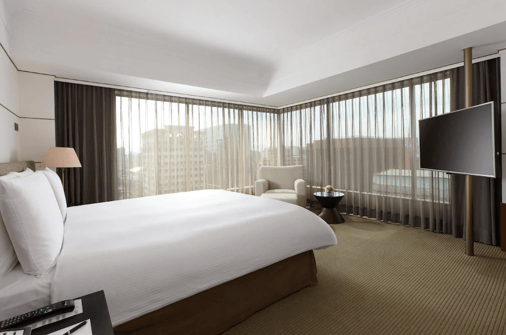 "台北親子飯店"【台北車站住宿】台北晶華酒店的豪華角落客房，配備大床與環繞式落地窗，採光極佳，可俯瞰台北城市景色。房內設計簡約時尚，擁有懸掛式電視、柔和色調的地毯及休憩沙發椅，營造高級感。