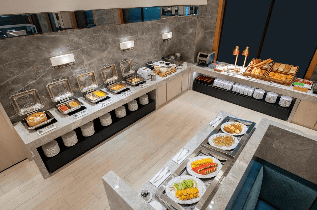 【松山機場住宿】「台北漢普頓酒店」自助早餐區，裝潢高級現代，設有各式中西式早餐，包括水果、糕點、熱食與現烤麵包。擺盤精緻，環境寬敞明亮，提供豐富的用餐選擇。