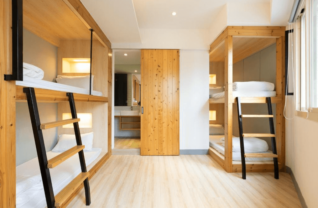 【西門町住宿】台北漫步旅店的四人房，採用木製上下舖設計，每個床位均設有獨立閱讀燈與插座，營造出溫馨的住宿環境。房內配有木質拉門通往乾溼分離的衛浴區，整體空間明亮且舒適。