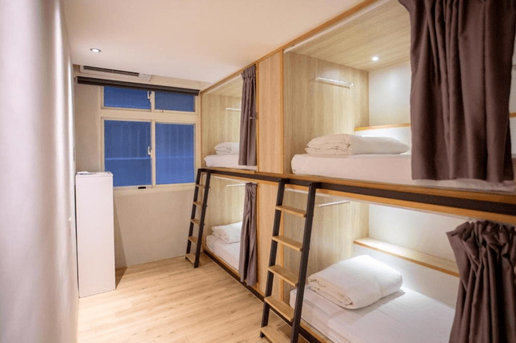 【西門町住宿】台北漫步旅店的房型，房內設有上下舖床位，每個床位皆附有獨立窗簾、閱讀燈與收納空間，提供旅客隱私與舒適的住宿體驗。房間內設有木質地板與簡約裝飾，營造出溫暖且實用的環境。