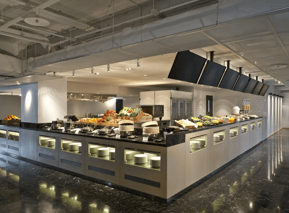 台北西門町意舍酒店的自助早餐區，提供豐富的食材，包括新鮮水果、沙拉、麵包與熟食料理。寬敞的餐檯設有黑色大理石檯面，白色瓷磚背景讓空間更加明亮整潔，開放式廚房設計讓用餐環境更具互動感。