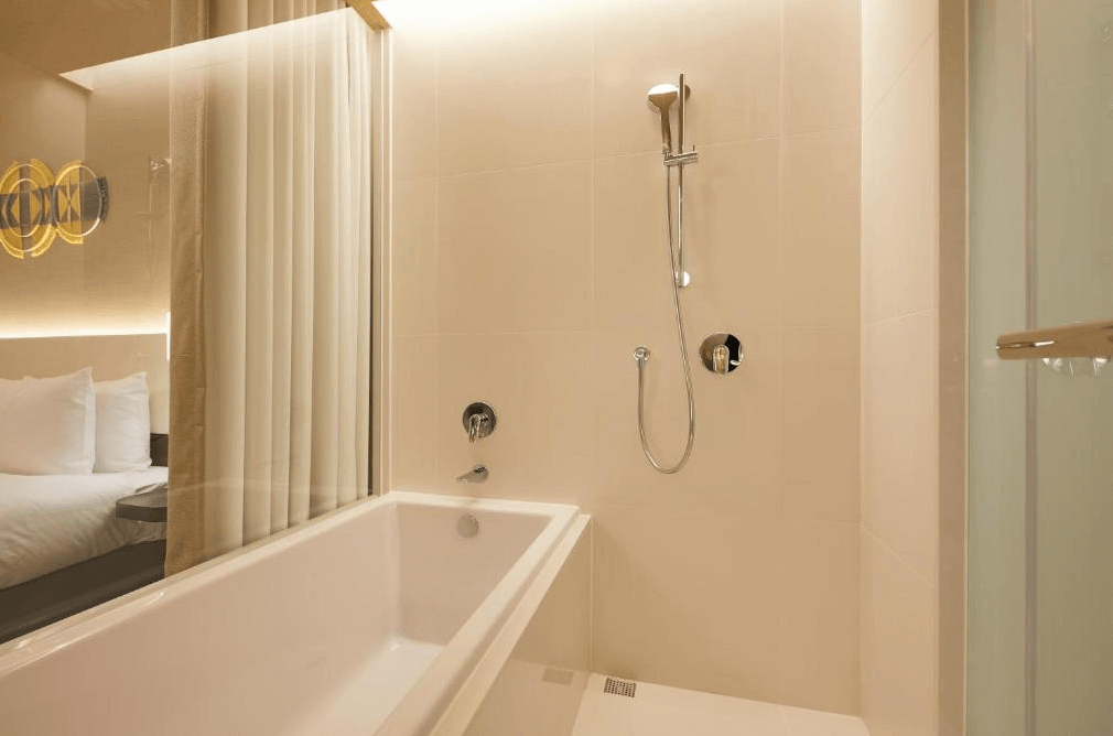 【台北親子飯店】和苑三井花園飯店台北忠孝的浴室，設計簡約溫馨，採用米白色系，搭配浴缸與淋浴設備。透明玻璃與浴簾設計讓空間更顯寬敞，房內的柔和燈光增添放鬆氛圍。