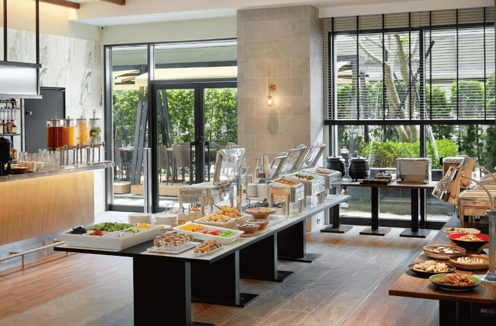 【台北親子飯店】和苑三井花園飯店台北忠孝的自助早餐餐廳，空間寬敞明亮，擁有大面落地窗與戶外綠景。餐台上擺滿各式精緻早餐，包括沙拉、麵包、熟食、熱湯與果汁，提供豐富的餐飲選擇，滿足不同旅客的需求。