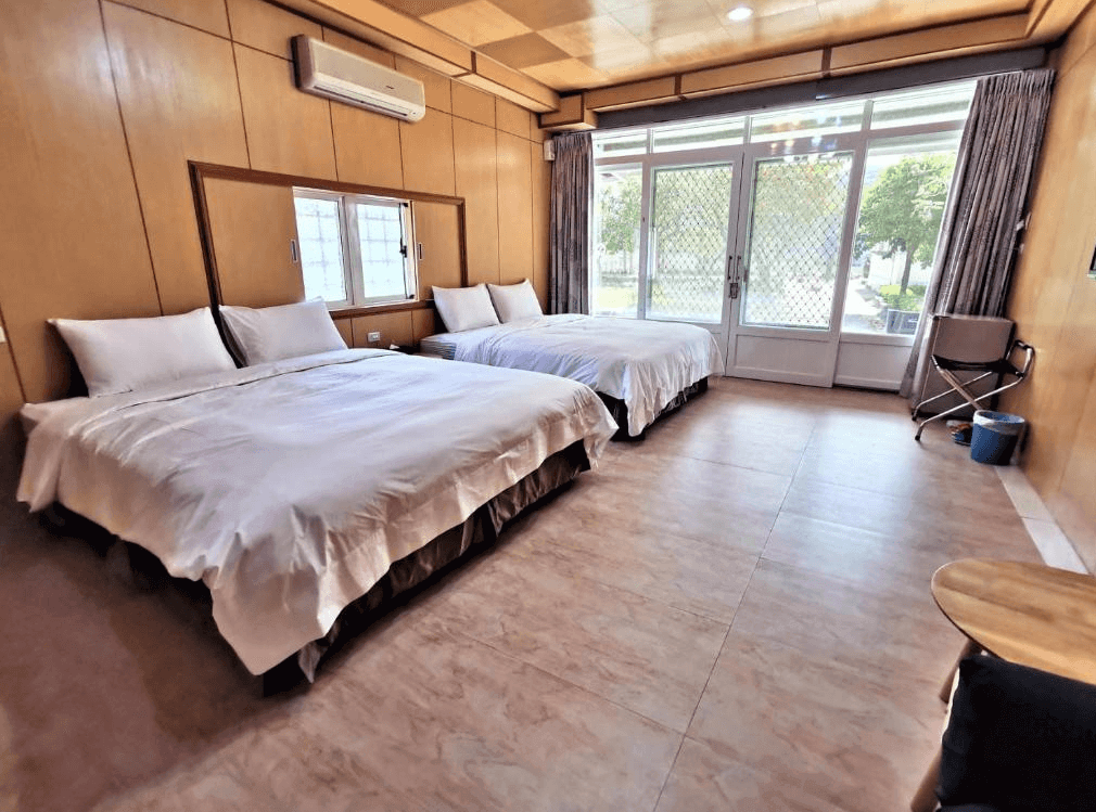 【四重溪溫泉】四重溪可以居民宿的家庭房，內部設有兩張大床，適合多人入住。房內採木質裝潢與簡約設計，搭配白色寢具，營造溫馨放鬆的氛圍。大片玻璃門窗連接戶外庭院，讓房內擁有充足採光。牆上裝有冷氣，提供舒適的居住環境。