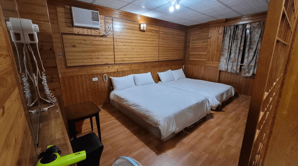 【四重溪溫泉】四重溪洺泉溫泉旅館的四人房，內部以溫暖的木質裝潢為主，牆面與天花板皆採用木紋設計，帶來自然舒適感。房內設有兩張大床，搭配白色寢具，空間寬敞。窗戶採用懷舊窗簾，讓整體風格更具復古韻味。牆上裝有冷氣，提供舒適的入住環境，並配有吹風機與基本備品。