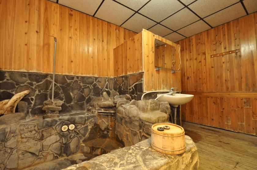 【四重溪溫泉】四重溪洺泉溫泉旅館的溫泉浴室，內部設有獨特的石砌泡湯池，並搭配木質牆面，營造日式溫泉風格。浴池以天然石材鋪設，呈現原始質樸的氛圍。牆上設有簡約洗手台與鏡子，空間感寬敞，可提供私密且放鬆的泡湯體驗。