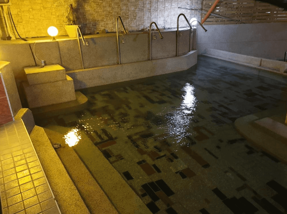 【四重溪溫泉】四重溪洺泉溫泉旅館的溫泉池，池水波光粼粼，映照出溫暖的燈光。池邊設有階梯與金屬扶手，方便遊客進出浴池。周圍以石牆與木質隔板裝飾，增添傳統日式湯屋的氛圍。夜間燈光柔和，營造靜謐放鬆的泡湯環境。