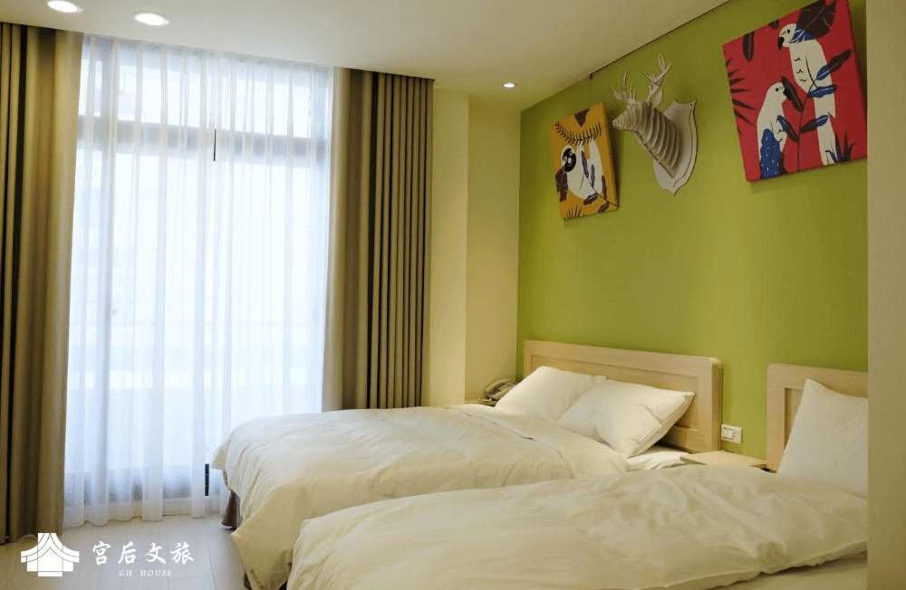 【鹿港住宿】"彰化飯店"宮后文旅的雙人床房，房間的牆面上有充滿色彩的藝術畫作，並且選用了溫暖的綠色背景，增添了活力。大窗戶讓自然光透過，營造出明亮而舒適的睡眠空間。