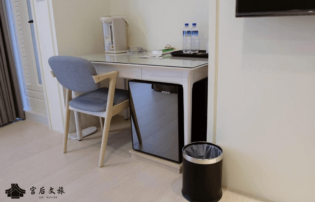 【鹿港住宿】"彰化飯店"宮后文旅的工作區域，這裡設有簡潔的桌椅和一些生活用品，如熱水壺和瓶裝水，這些設施為住客提供了便利的服務。這個空間保持簡約和實用，適合休息或工作。