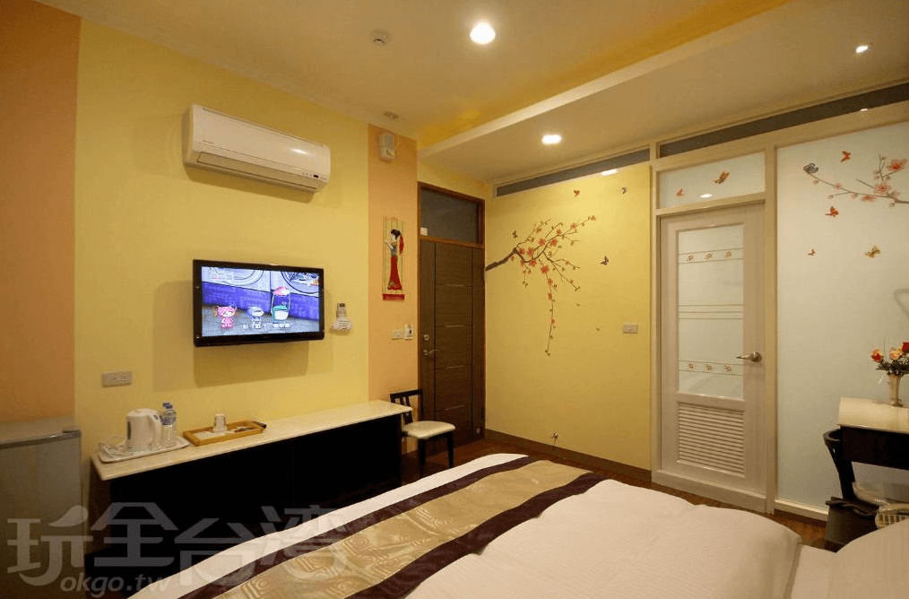 【集集火車站住宿】富麗渡假民宿的溫馨雙人房，牆面以淡黃色調點綴手繪樹枝與蝴蝶圖案，增添浪漫感。房內配有壁掛式電視、小型冰箱與茶水設備，整體設計簡約舒適，適合休閒度假入住。