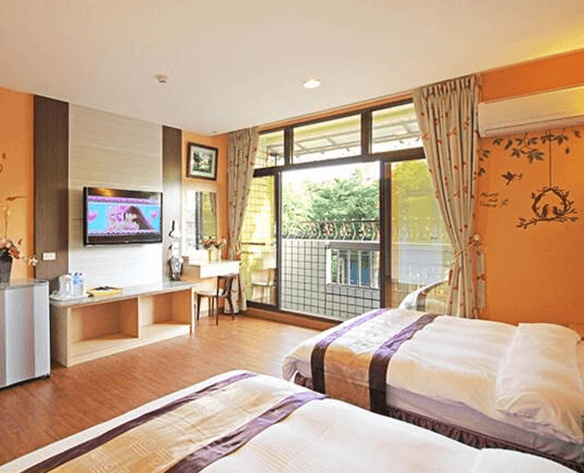 【集集火車站住宿】富麗渡假民宿的雙床房，牆面以溫暖橘色調與可愛的鹿與樹枝壁貼點綴，增添趣味感。落地窗讓房間更加明亮，陽台外可見綠意盎然的庭院景觀，整體空間寬敞舒適。