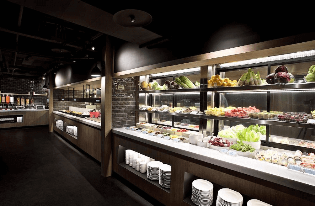 【西門町住宿】捷絲旅台北西門館的自助早餐區，擺滿新鮮蔬果與多樣化的餐點，採用現代感木質裝潢搭配燈光點綴，提供豐富且健康的用餐選擇。