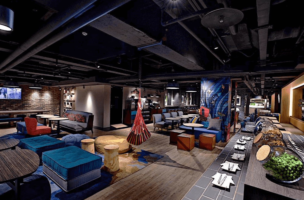 【西門町住宿】捷絲旅台北西門館的公共休憩區，結合工業風與現代藝術設計，擺放多種舒適沙發、木質桌椅，並以彩繪裝飾柱、吊椅增添活力感，適合作為旅客放鬆或社交的空間。