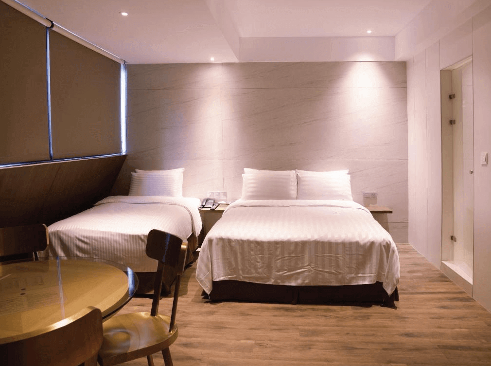 【台北車站住宿】（旅樂序精品旅館 站前五館）：家庭房設計，內部配置一張雙人床與一張單人床，搭配木地板與淺色大理石紋牆面，呈現簡約溫馨氛圍。房內設有餐桌與木質椅子，適合家庭或多人入住。