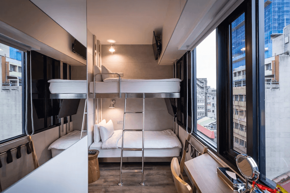 【台北車站住宿】（旅樂序精品旅館 站前五館）：現代感膠囊風格客房，採用雙層床設計，搭配大片落地窗，可俯瞰都市景色。房內空間精巧，設有書桌與化妝鏡，適合背包客或商務旅客入住。