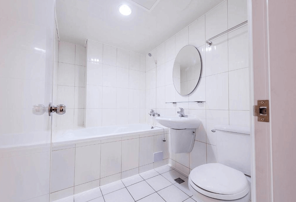 【西門町住宿】明日大飯店的浴室，整體採用白色瓷磚設計，乾淨明亮。浴室內設有浴缸、馬桶與洗手台，搭配圓形鏡子與簡約玻璃置物架，空間感十足且保持整潔。