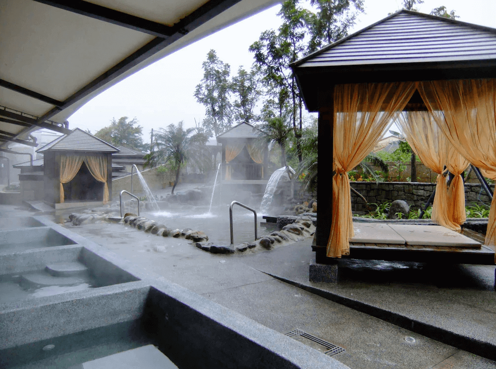 【金山溫泉】沐舍溫泉渡假酒店的露天溫泉區，設有多個石材泡湯池與水療設施，並搭配涼亭與紗簾，提供遮蔽與隱私。周圍環繞著熱帶植栽，瀰漫著溫泉蒸氣，營造出悠閒愜意的氛圍，是放鬆身心的理想場所。